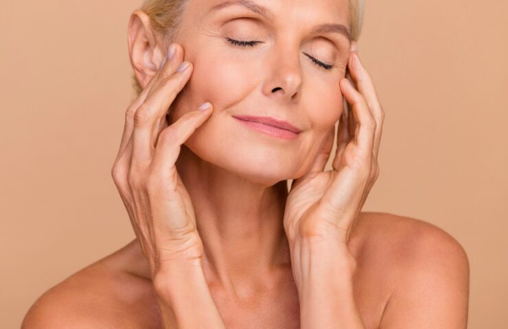 Woman with eyes closed gently touching her face, showing smooth, firm skin after using collagen moisturising cream