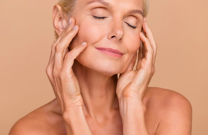 Woman with eyes closed gently touching her face, showing smooth, firm skin after using collagen moisturising cream