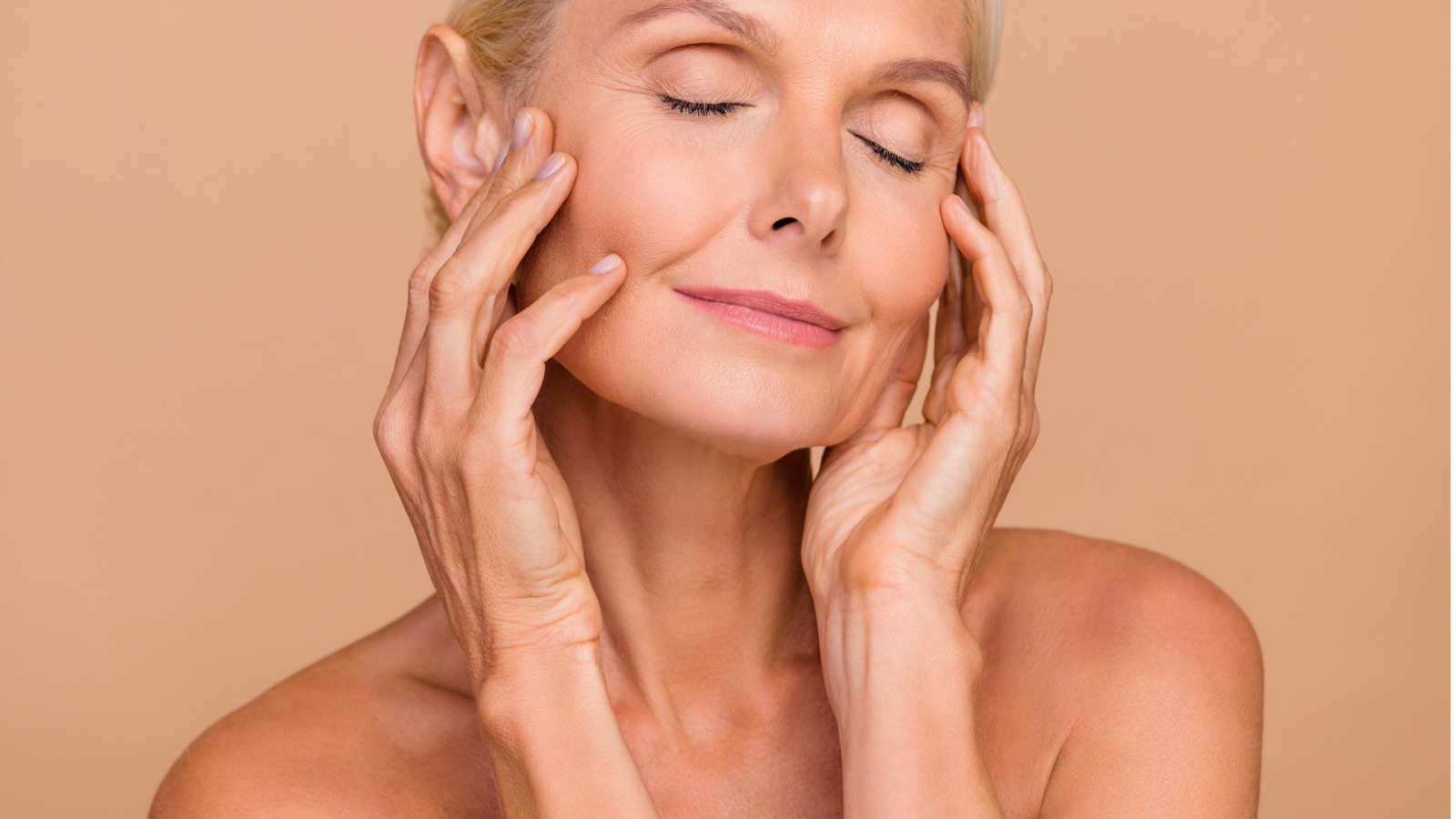 Woman with eyes closed gently touching her face, showing smooth, firm skin after using collagen moisturising cream